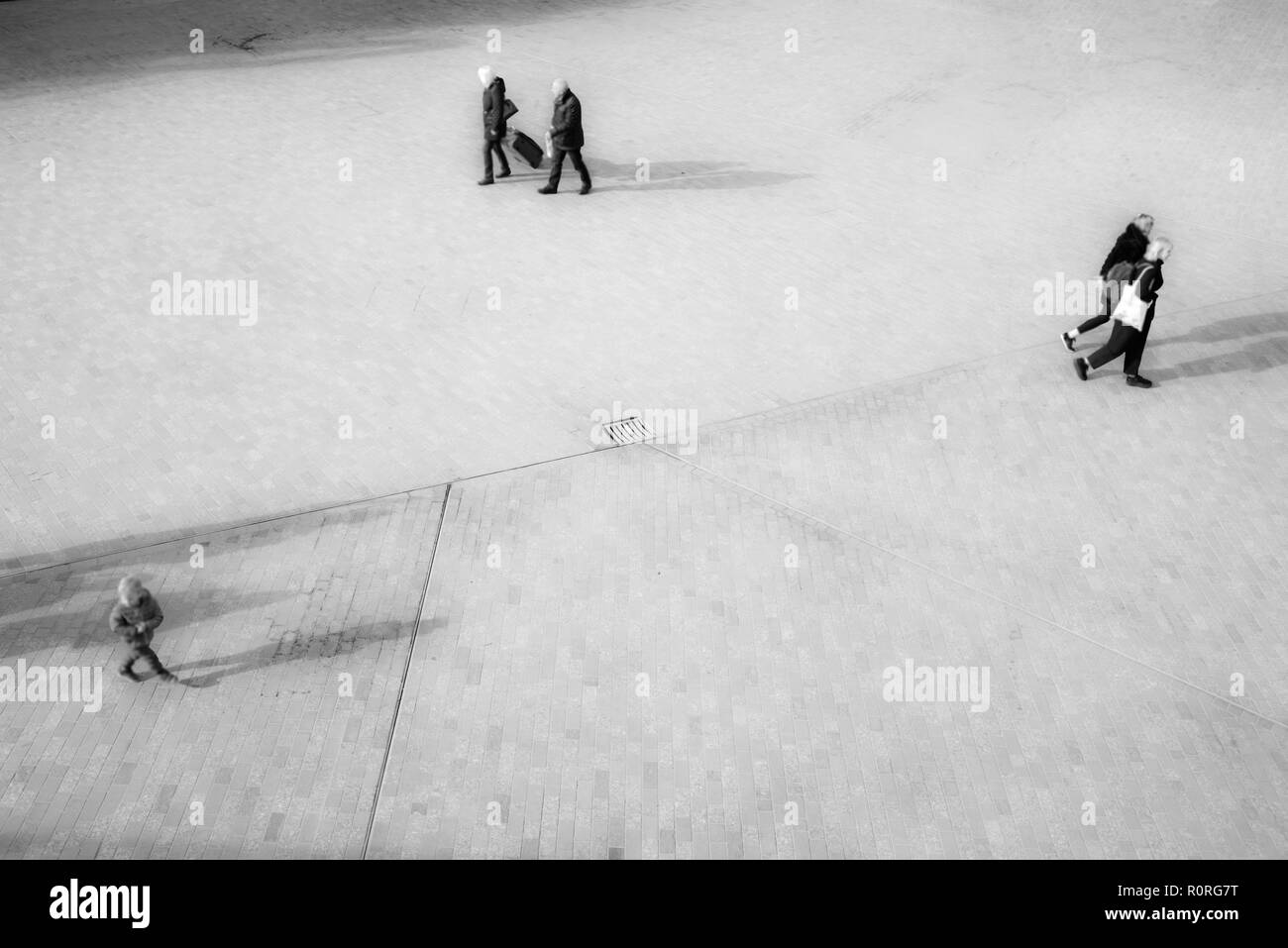 Blurred unrecognizable people from above walking on an open space square with shadows projecting on the floor Stock Photo