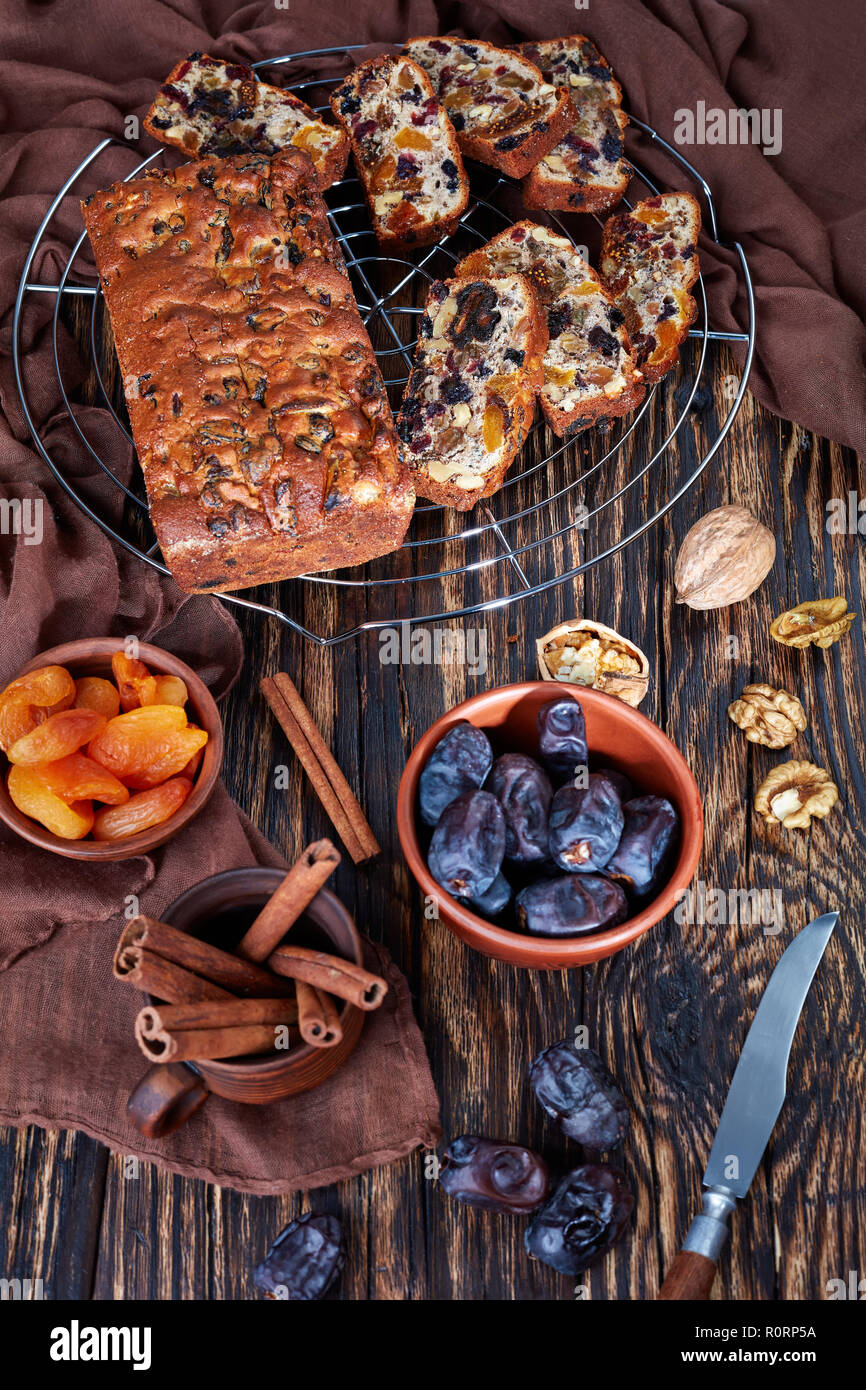 overhead view of delicious chunky dried fruits rich cake on a wire cake stand with brown cloth, cinnamon sticks, dried apricots and date fruits on a r Stock Photo