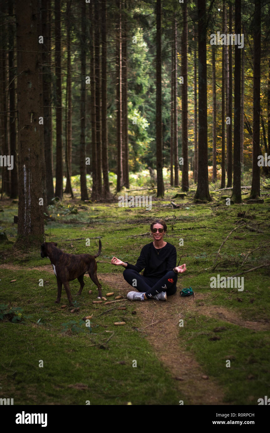 young woman sitting on the ground in a green forest doing yoga Stock Photo