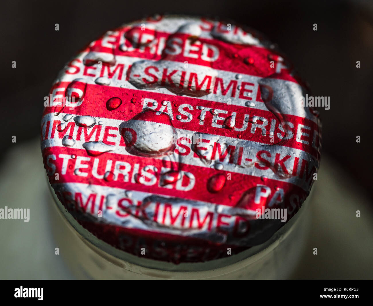 Milk Bottle Top - Semi Skimmed Pasteurised Red and Silver Milk Bottle top with raindrops pooled on top Stock Photo