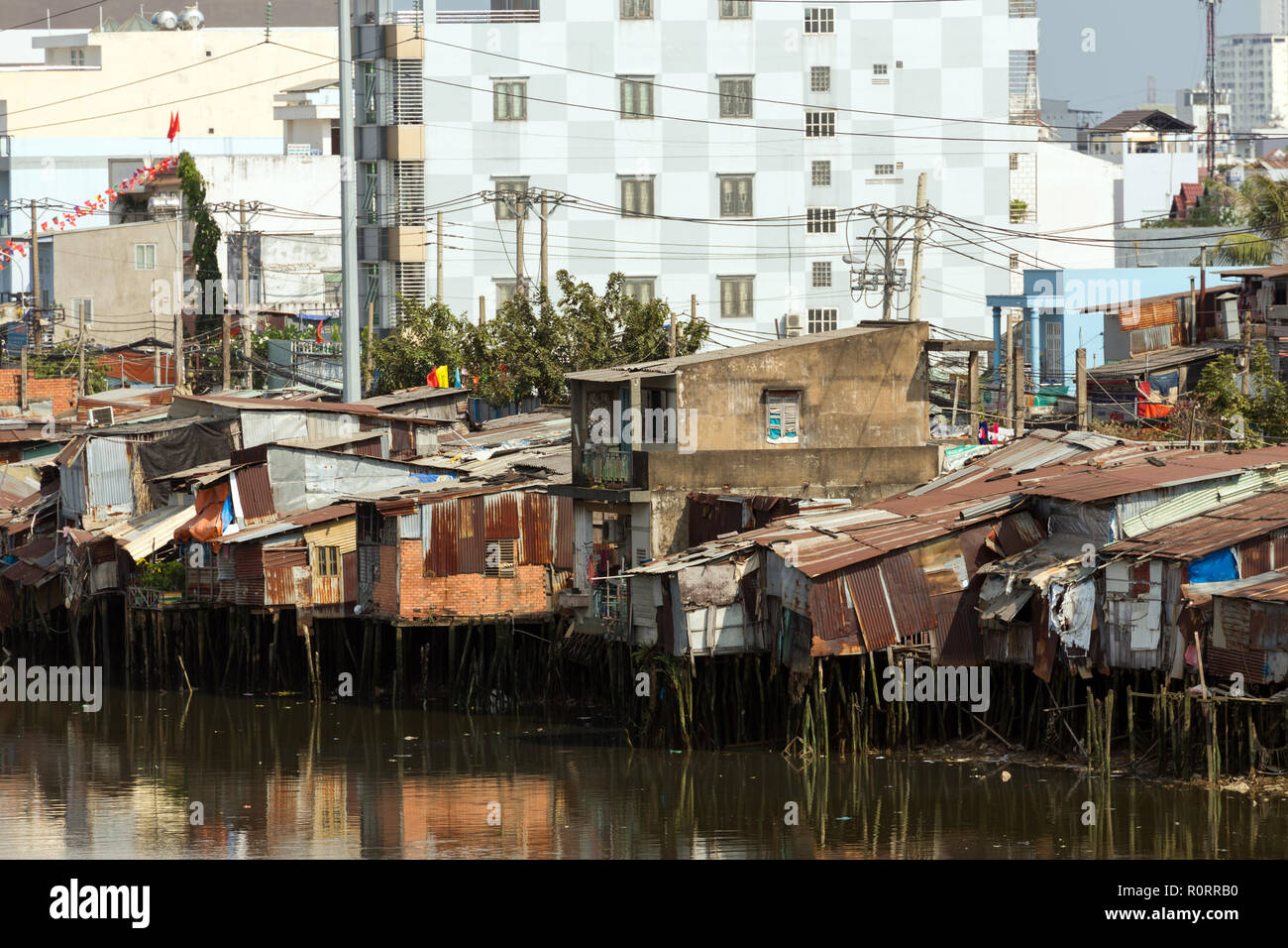 Slum wooden house on the Saigon river bank, in front of modern