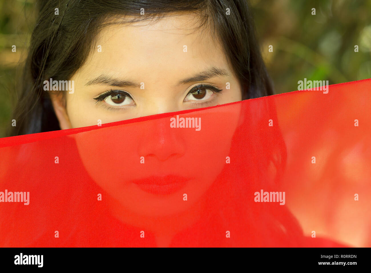 Vietnamese woman peeking over red fabric at the camera Stock Photo