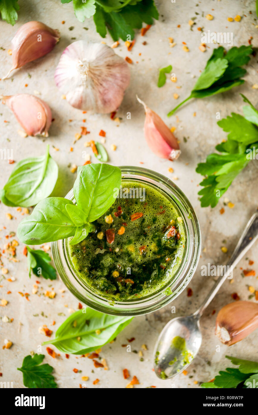 Argentinian traditional food, raw homemade green Chimichurri salsa or sauce woth parsley, garlic, basil leaves, hot pepper and spices, light stone tab Stock Photo