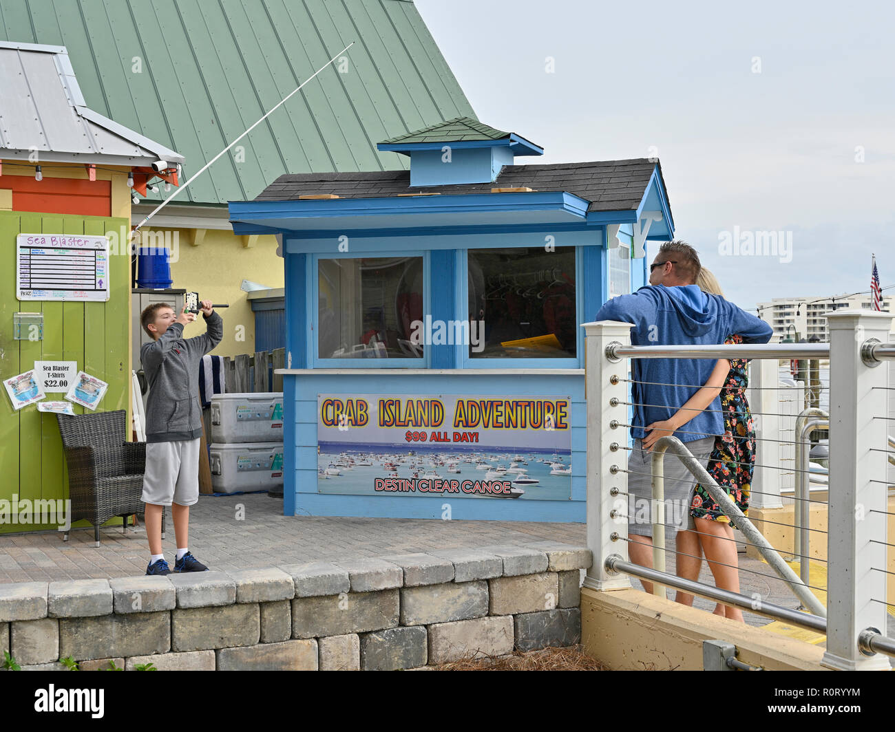 Young male boy taking a picture or a photo of an adult couple or parents at the tourist resort HarborWalk Village and Marina in Destin Florida USA. Stock Photo