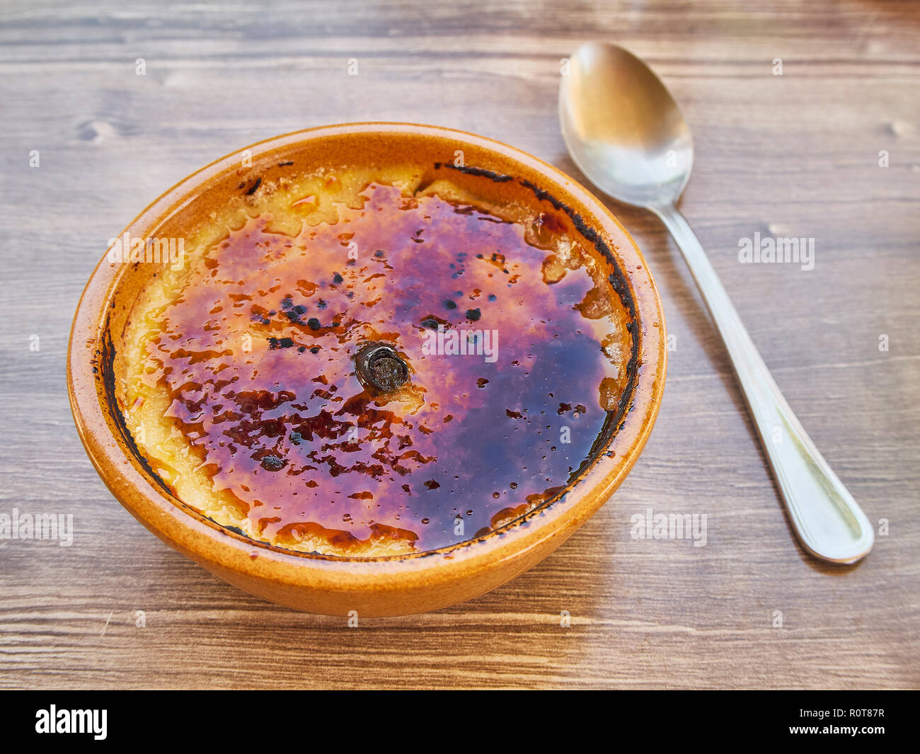 Crema Catalana or Creme Brulee in rustic bowl, typical taberna or bistro presentation with a cinnamon stick in the middle. Stock Photo