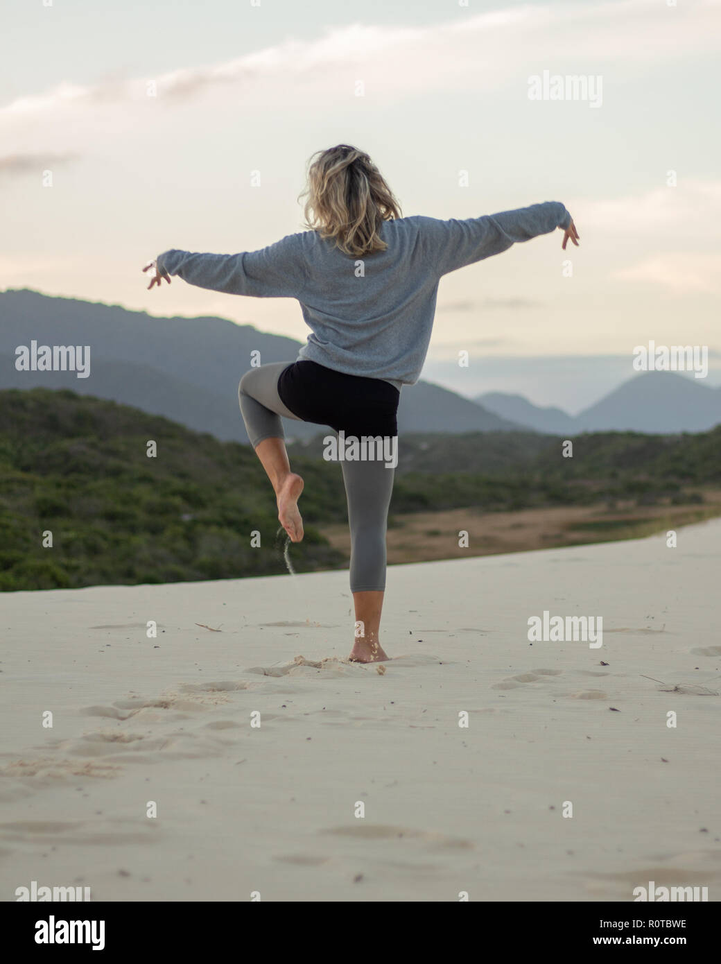 blonde woman with casual clothes jumping and dancing on a white sand dune Stock Photo