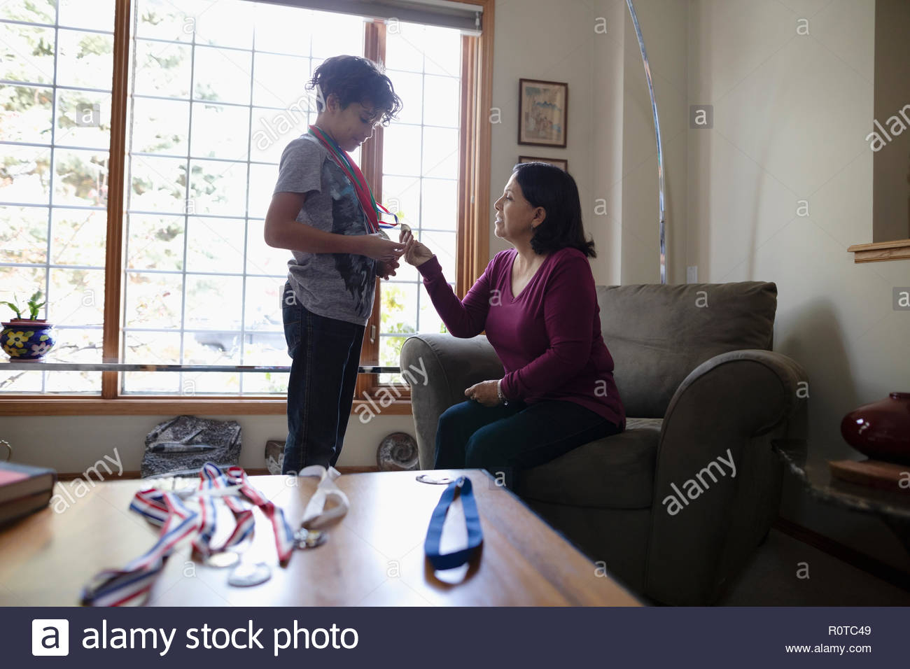 Latinx grandson showing sports medals to grandmother Stock Photo