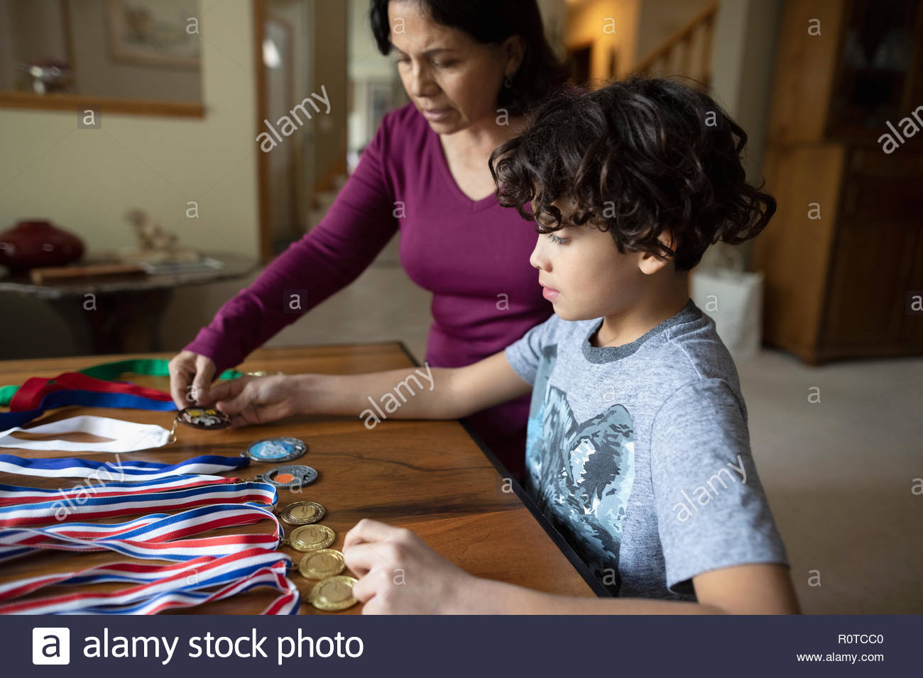 Latinx grandmother and grandson looking at sports medals Stock Photo