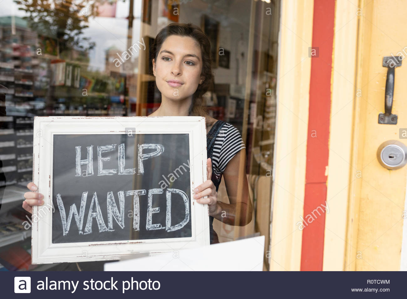 Female small business owner placing Help Wanted sign in shop window Stock Photo
