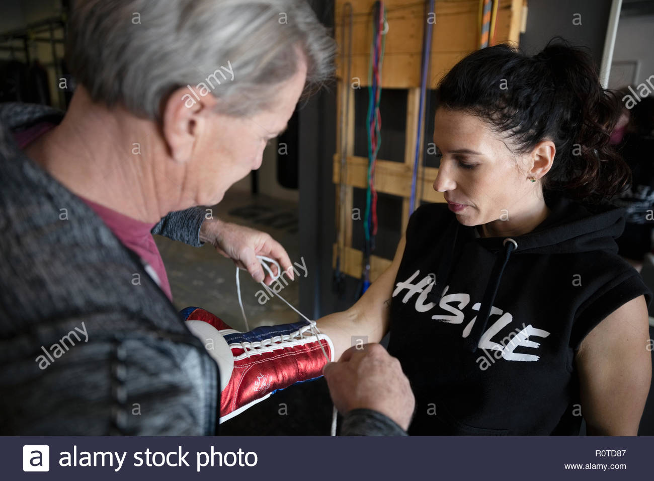 Trainer helping female boxer lacing boxing gloves in gym Stock Photo