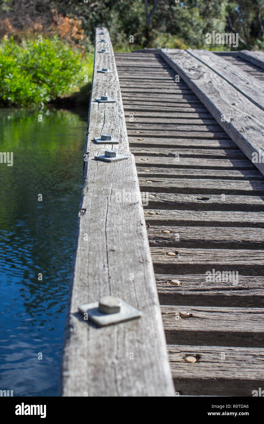 A low point of view (LPOV) of edge of rustic old wooden bridge crossing a river with iron rivets Stock Photo