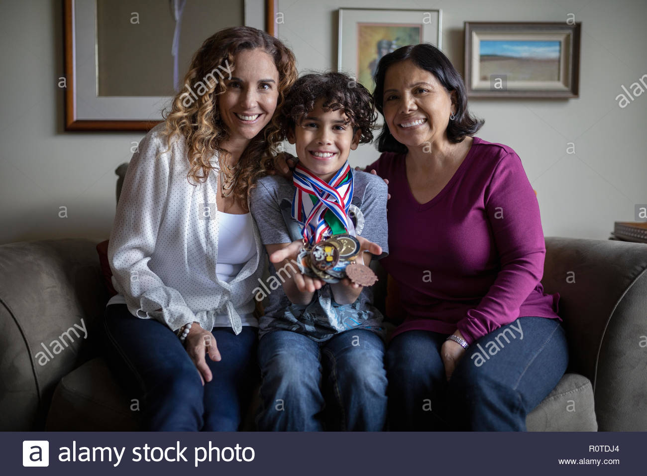 Portrait confident Latinx boy with sports medals sitting with mother and grandmother Stock Photo