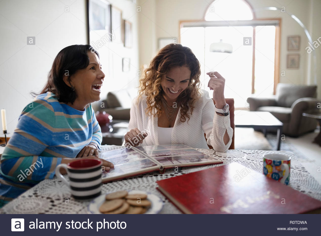 Happy Latinx daughter and senior mother looking at photo album Stock Photo