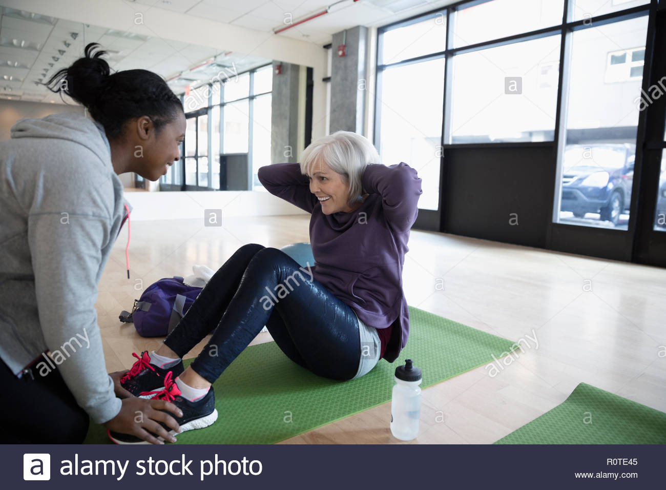 Personal trainer encouraging senior woman doing sit-ups in gym studio Stock Photo
