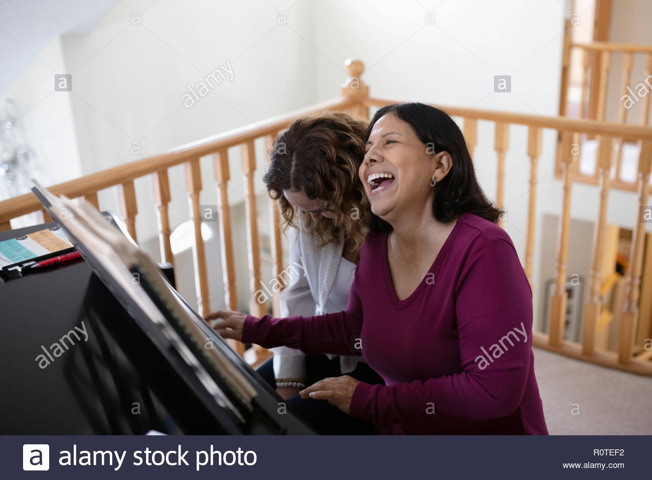 Happy, carefree Latinx daughter and senior mother plying piano Stock Photo