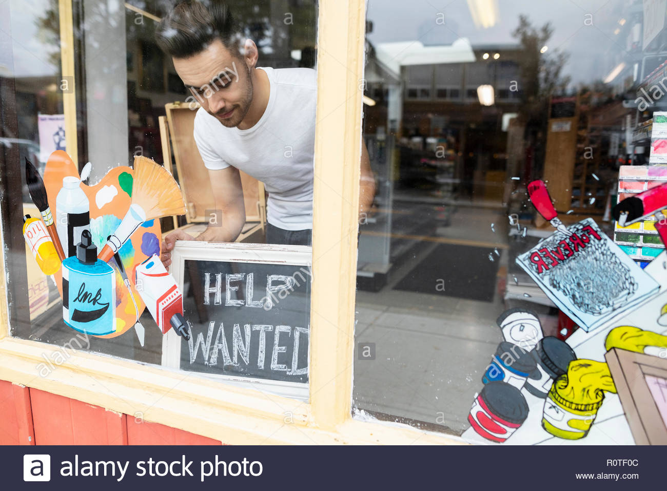 Male business owner placing Help Wanted sign in art supply shop window Stock Photo