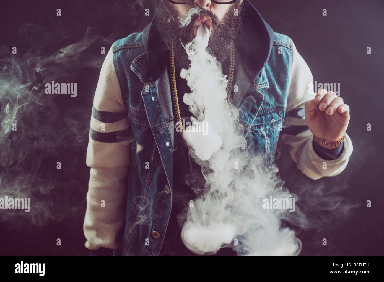 Young man with beard throwing a cloud of steam. Black background. Vaping an electronic cigarette with a lot of smoke Stock Photo