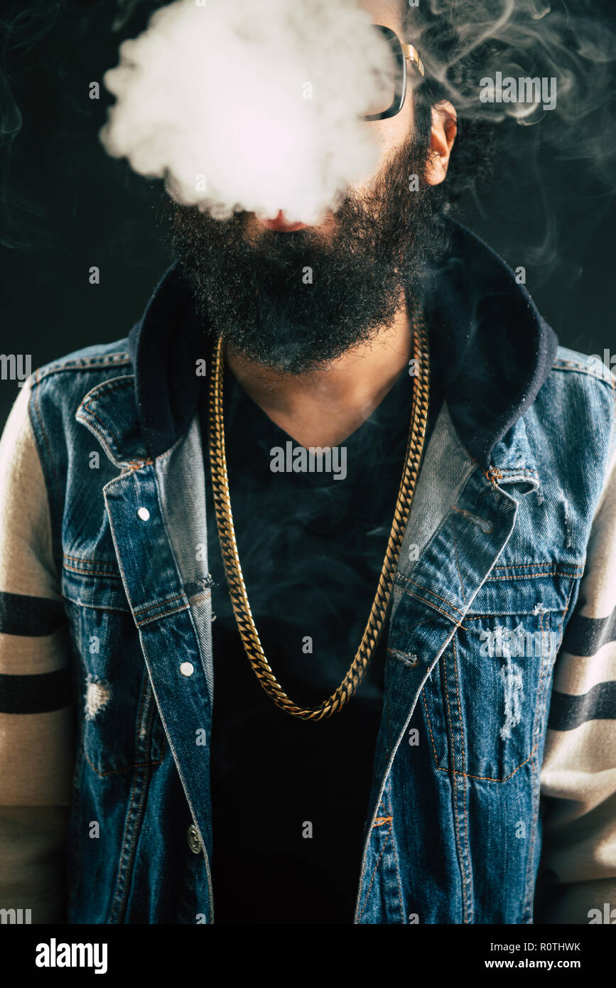 Young man with beard throwing a cloud of steam. Black background. Vaping an electronic cigarette with a lot of smoke Stock Photo