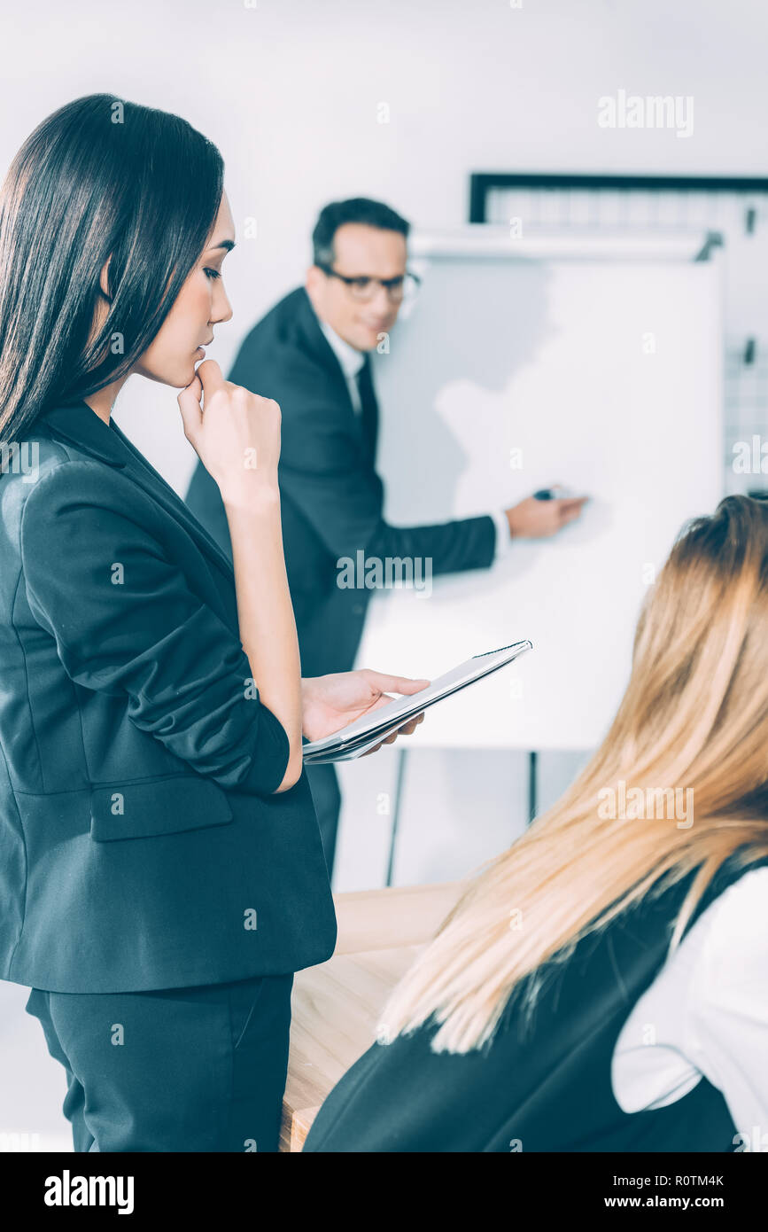 thoughtful asian businesswoman looking at notebook while her partner making presentation Stock Photo