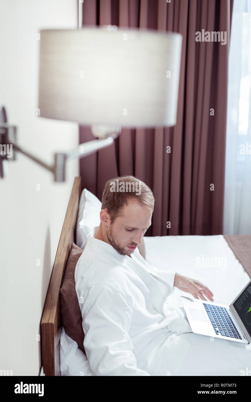 Blonde-haired businessman chilling on bed in luxurious hotel room Stock Photo