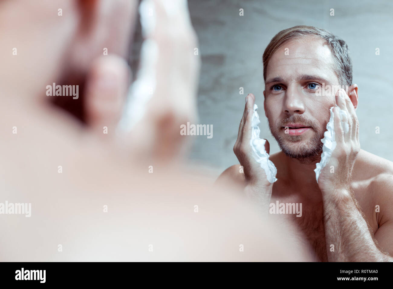 Handsome blue-eyed man using shaving foam while shaving face Stock Photo