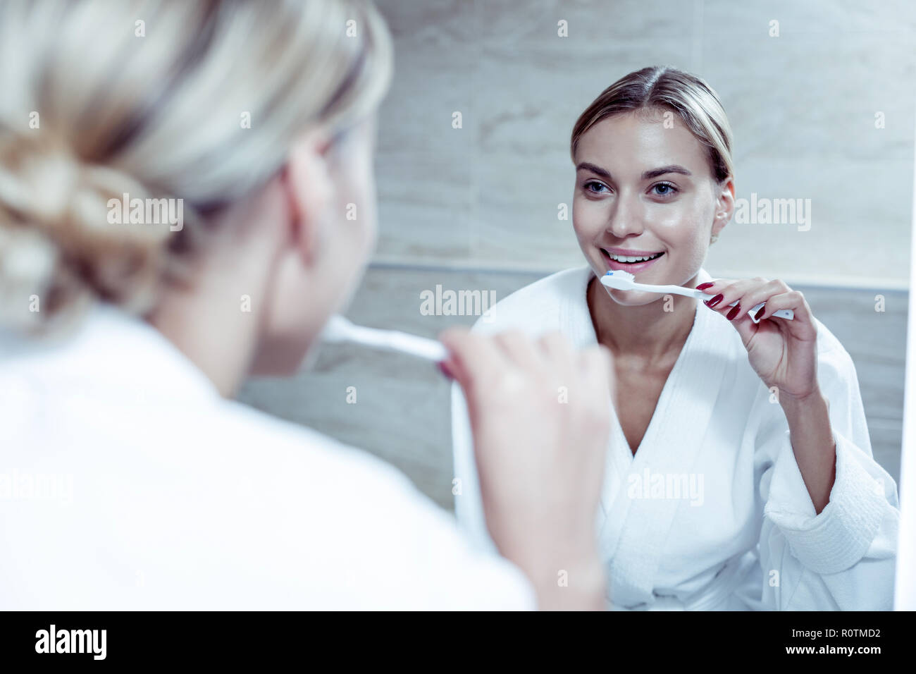 Beautiful blonde-haired woman wearing bathrobe brushing her teeth Stock Photo