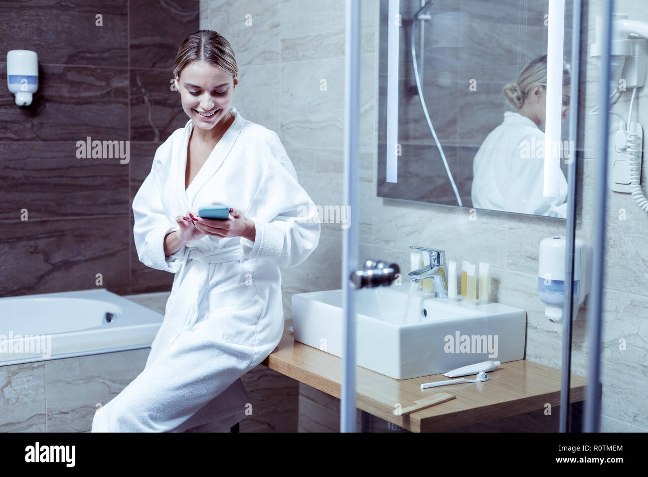 Blonde-haired woman reading message on phone standing in bathroom Stock Photo