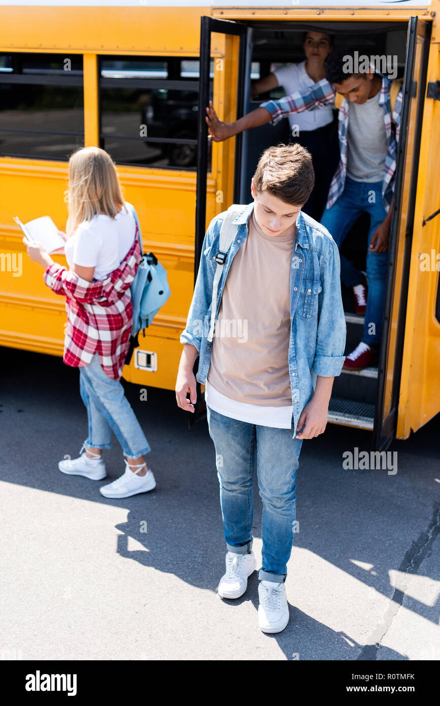 sad teenager standing in front of school bus with classmates Stock Photo - Alamy
