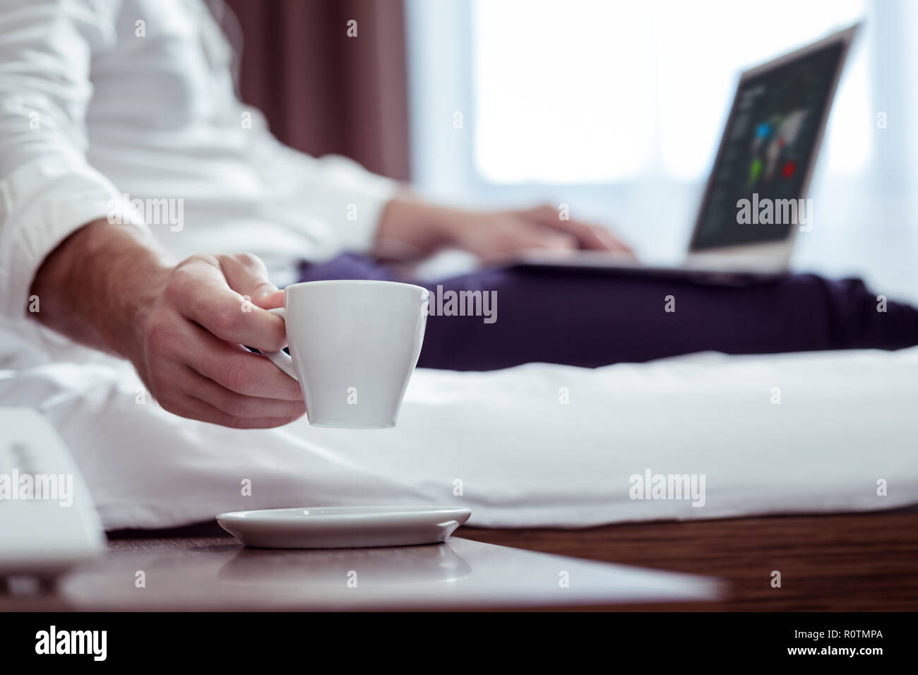 Businessman wearing suit lying on bed while drinking some tea Stock Photo