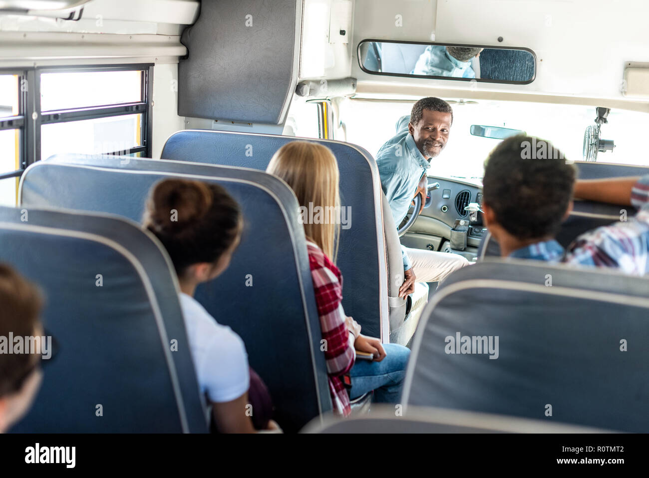 group of teen scholars riding school bus and talking with happy mature driver Stock Photo