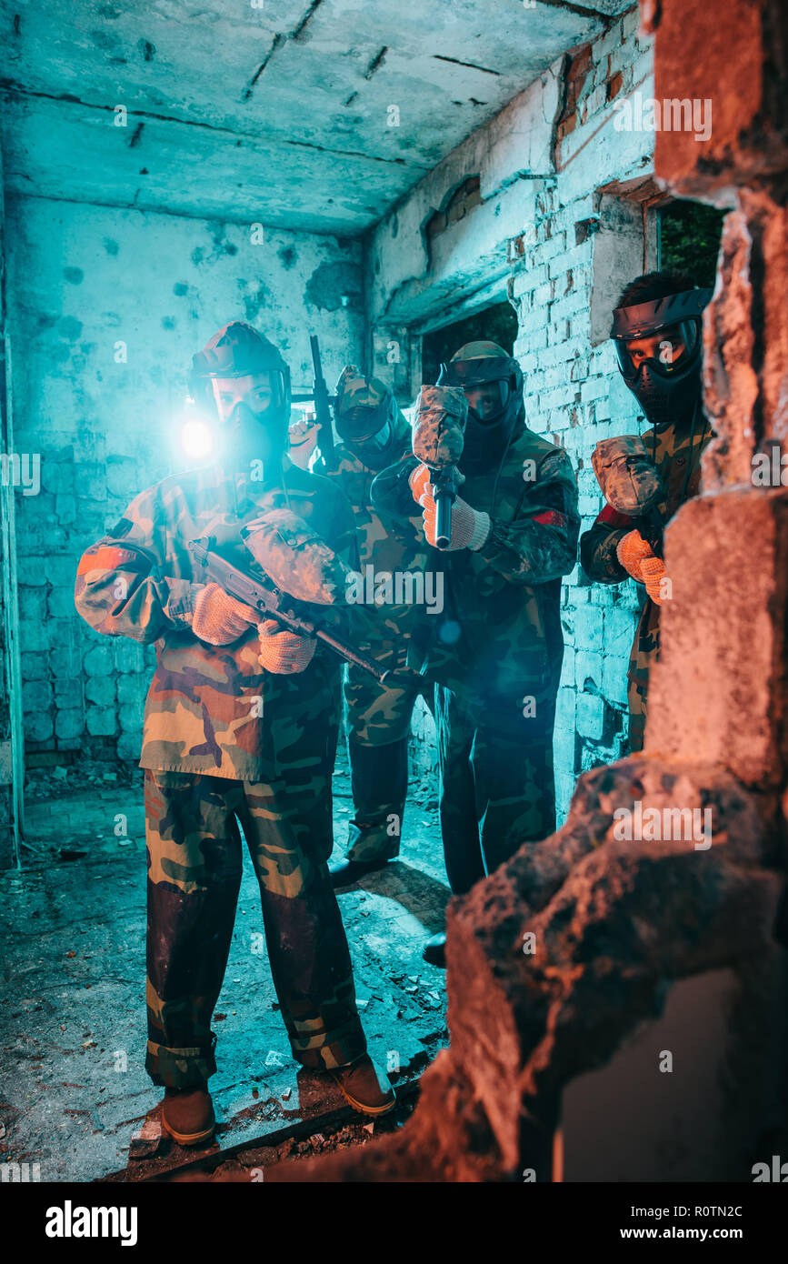 paintball team in uniform and protective masks with paintball guns in abandoned building Stock