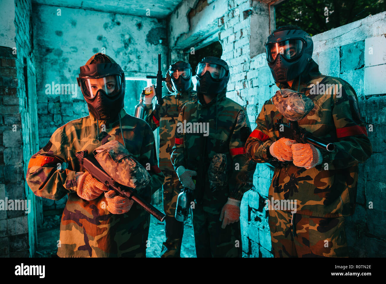 paintball team in uniform and protective masks standing with paintball guns in abandoned