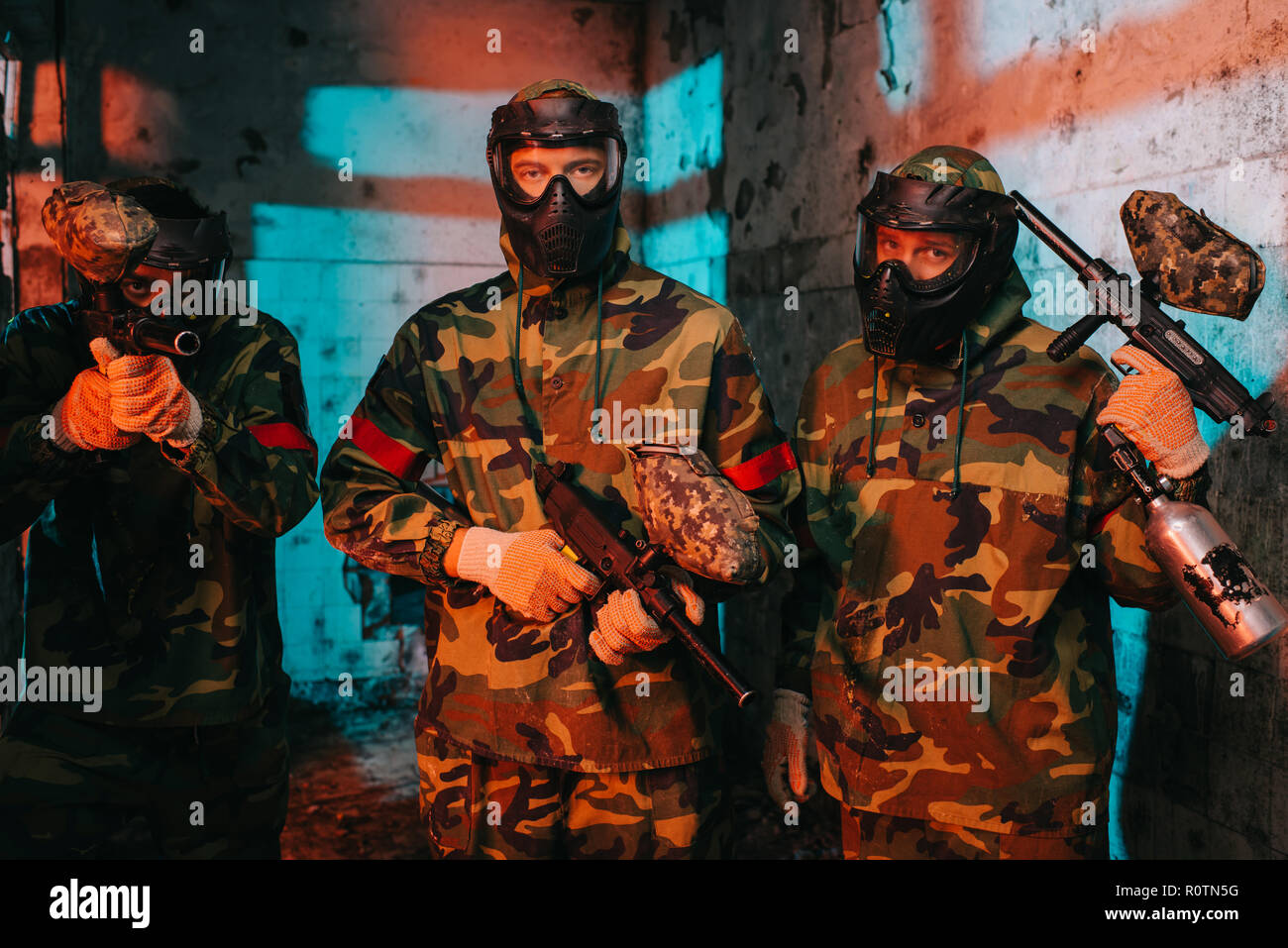 portrait of paintball team in uniform and protective masks with paintball guns in abandoned