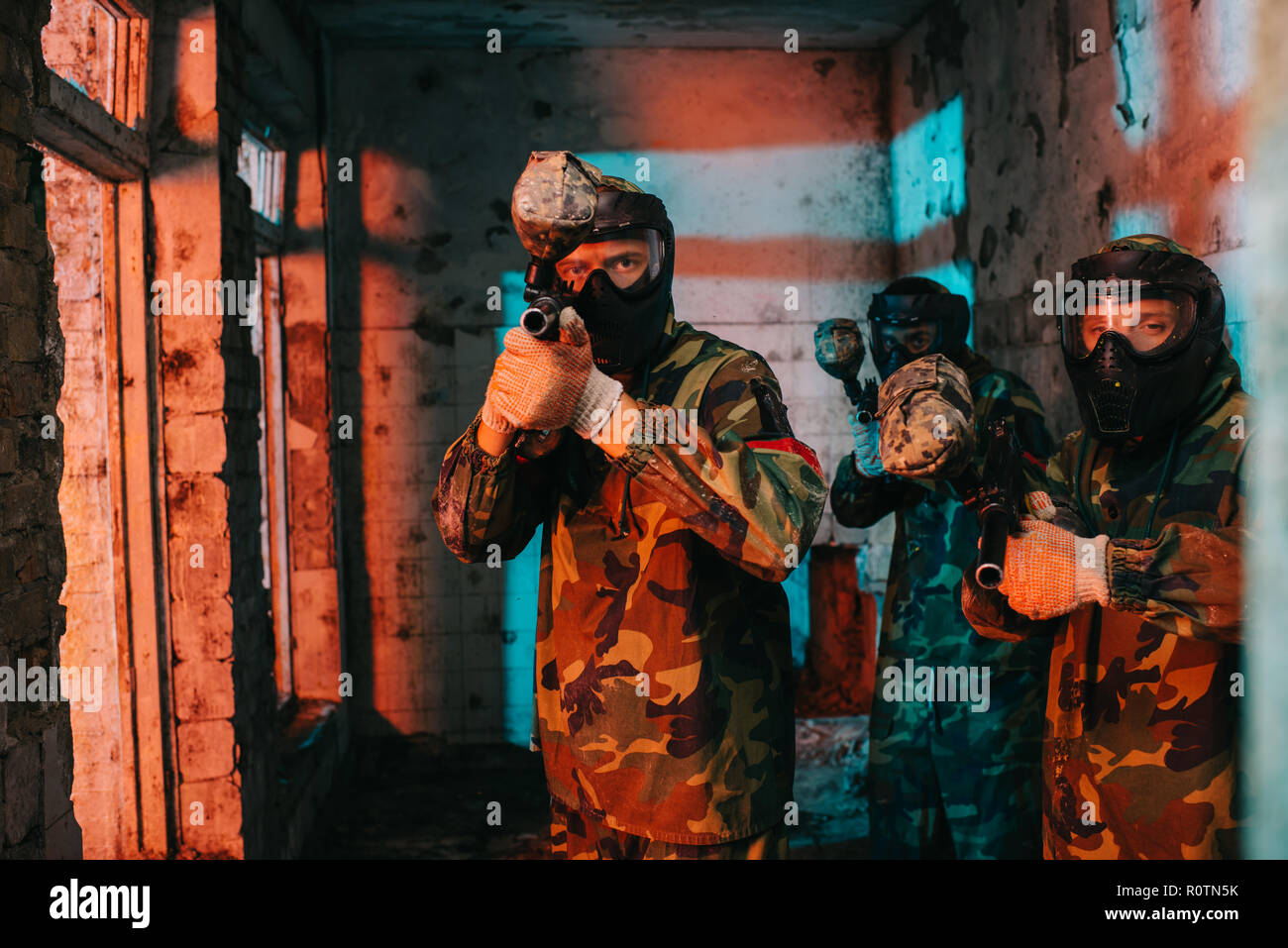 paintball team in uniform and protective masks aiming by paintball guns in abandoned building