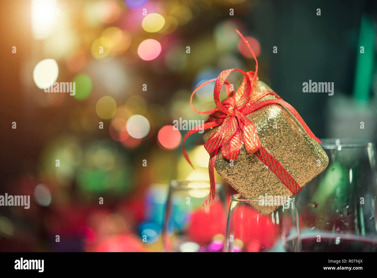 Christmas gift box or present with red bow ribbon on light bokeh blurred background. Copy space for greeting text. Cerebrate party concept. Stock Photo