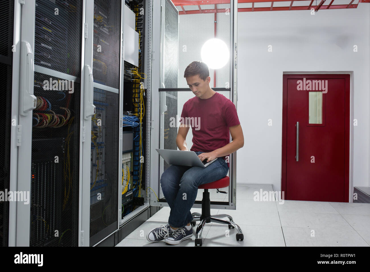 young man connecting wires in server cabinet while working with ...
