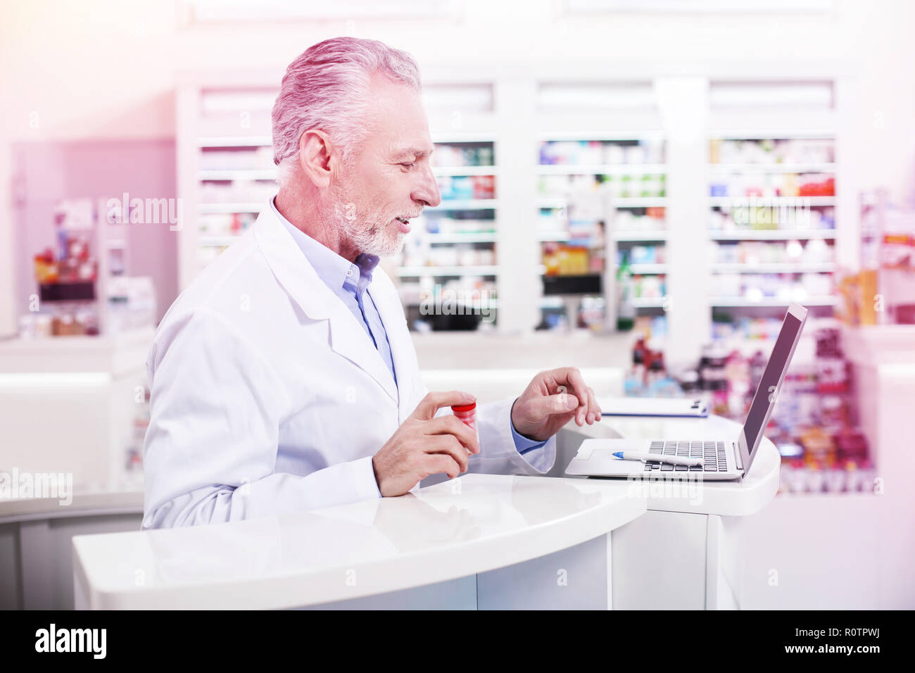 Elder grey-haired pharmacist working with a laptop Stock Photo