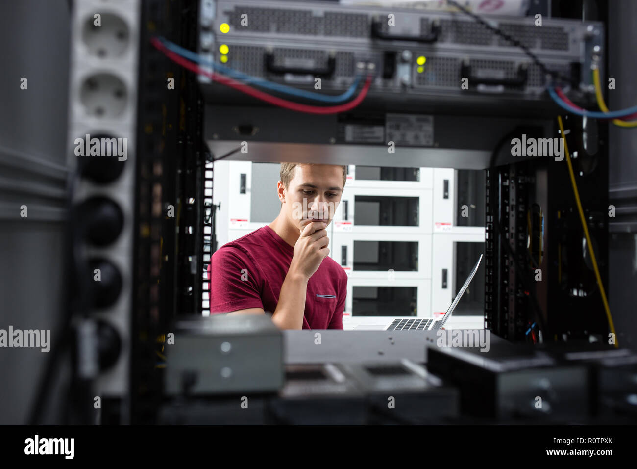 Male Server Engineer Works on a Laptop in Large Data Center. Stock Photo