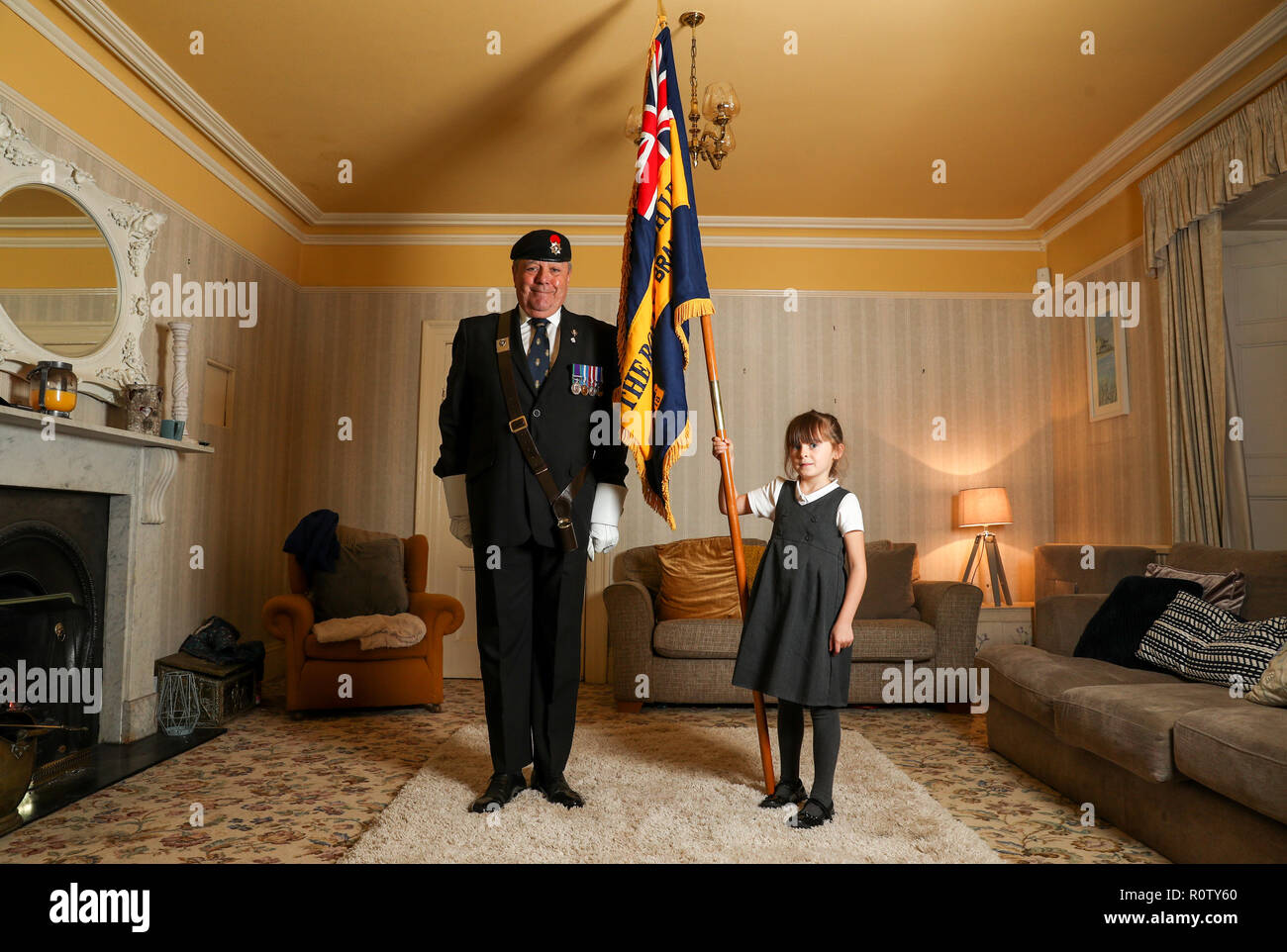Mollie Stonelake, seven, holds a full-size standard from the Torpoint & District Branch of the Royal British Legion alongside branch chairman Colin Prideaux, in her family home in Torpoint, Cornwall. Mollie went on her first parade aged five and will carry a specially-made miniature standard in a service on Sunday in her home town of Torpoint in Cornwall. Stock Photo