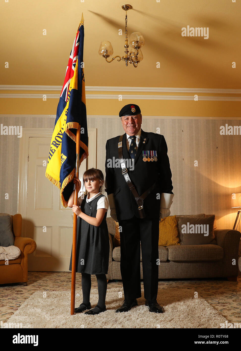 Mollie Stonelake, seven, holds a full-size standard from the Torpoint & District Branch of the Royal British Legion alongside branch chairman Colin Prideaux, in her family home in Torpoint, Cornwall. Mollie went on her first parade aged five and will carry a specially-made miniature standard in a service on Sunday in her home town of Torpoint in Cornwall. Stock Photo