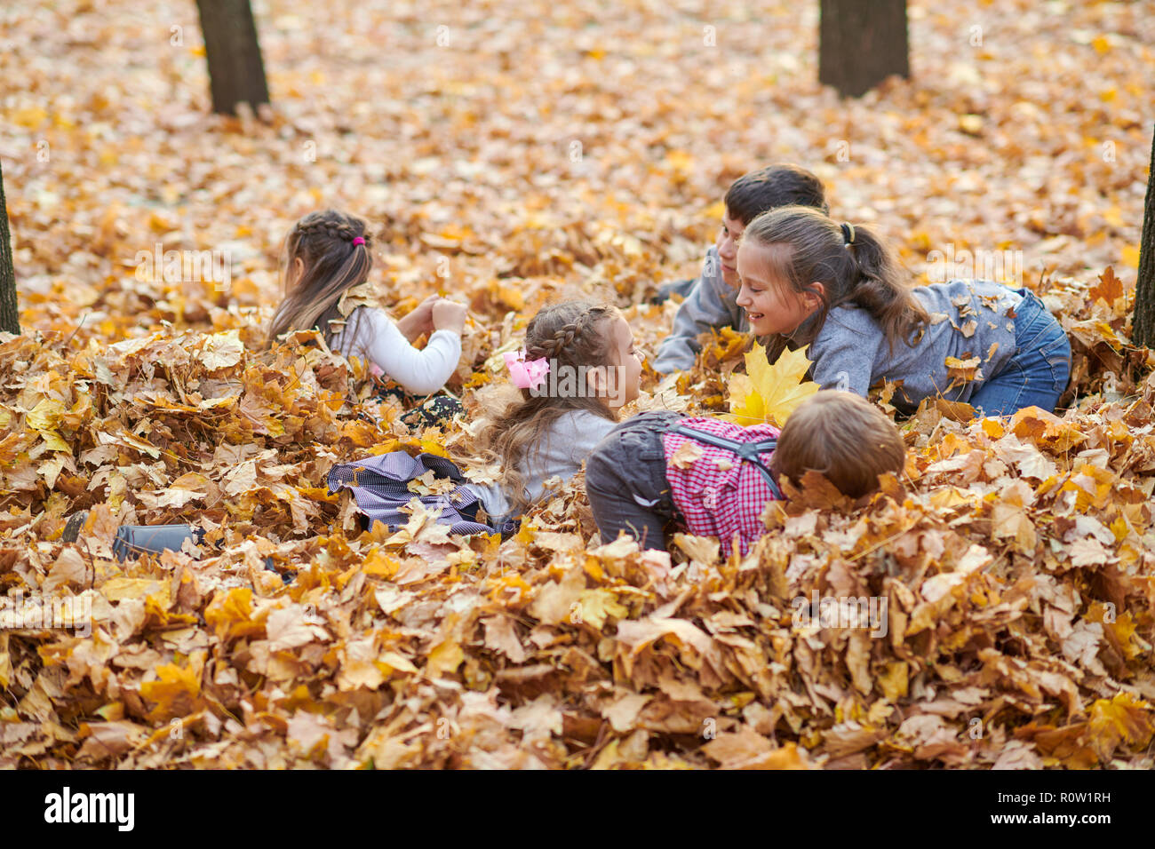 Children are lying and playing on fallen leaves in autumn city park ...