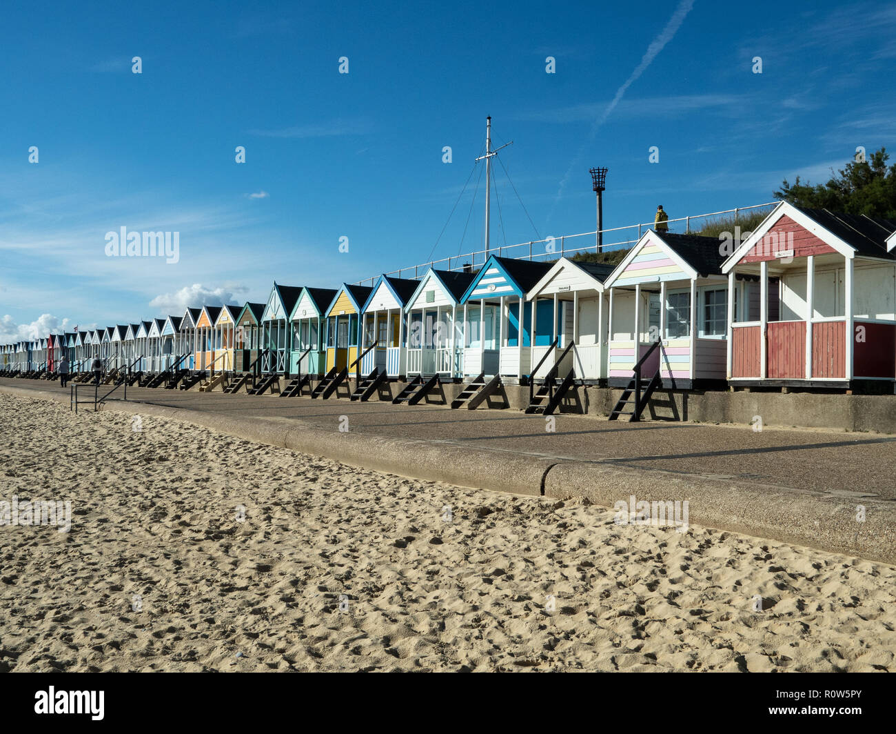 A row of brightly coloured beach huts along the seafront at Southwold against a bright blue sky Stock Photo