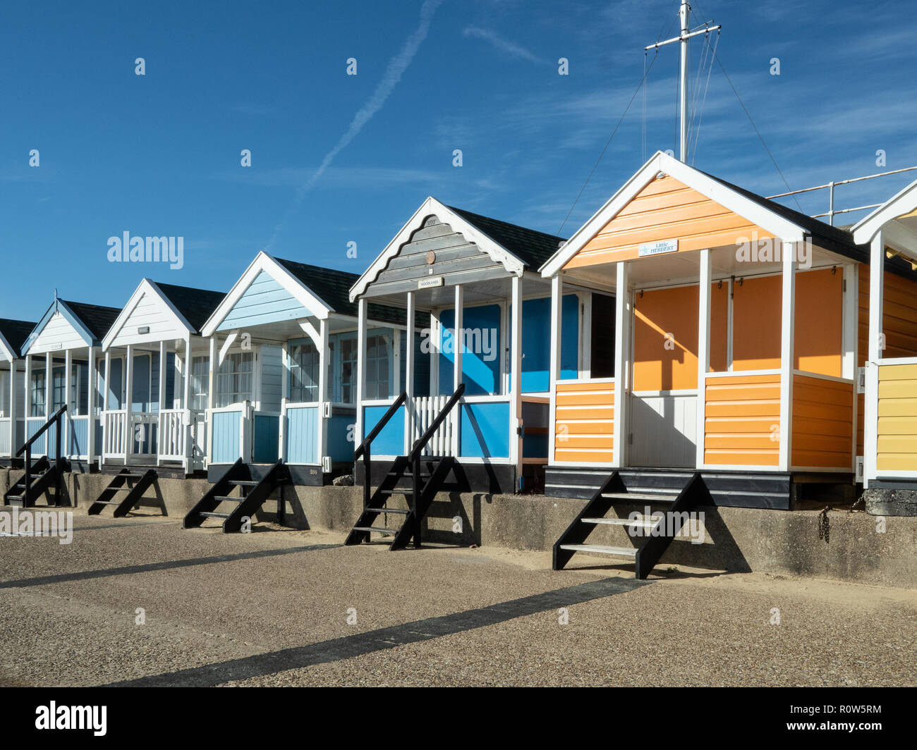 A row of brightly coloured beach huts along the seafront at Southwold against a bright blue sky Stock Photo