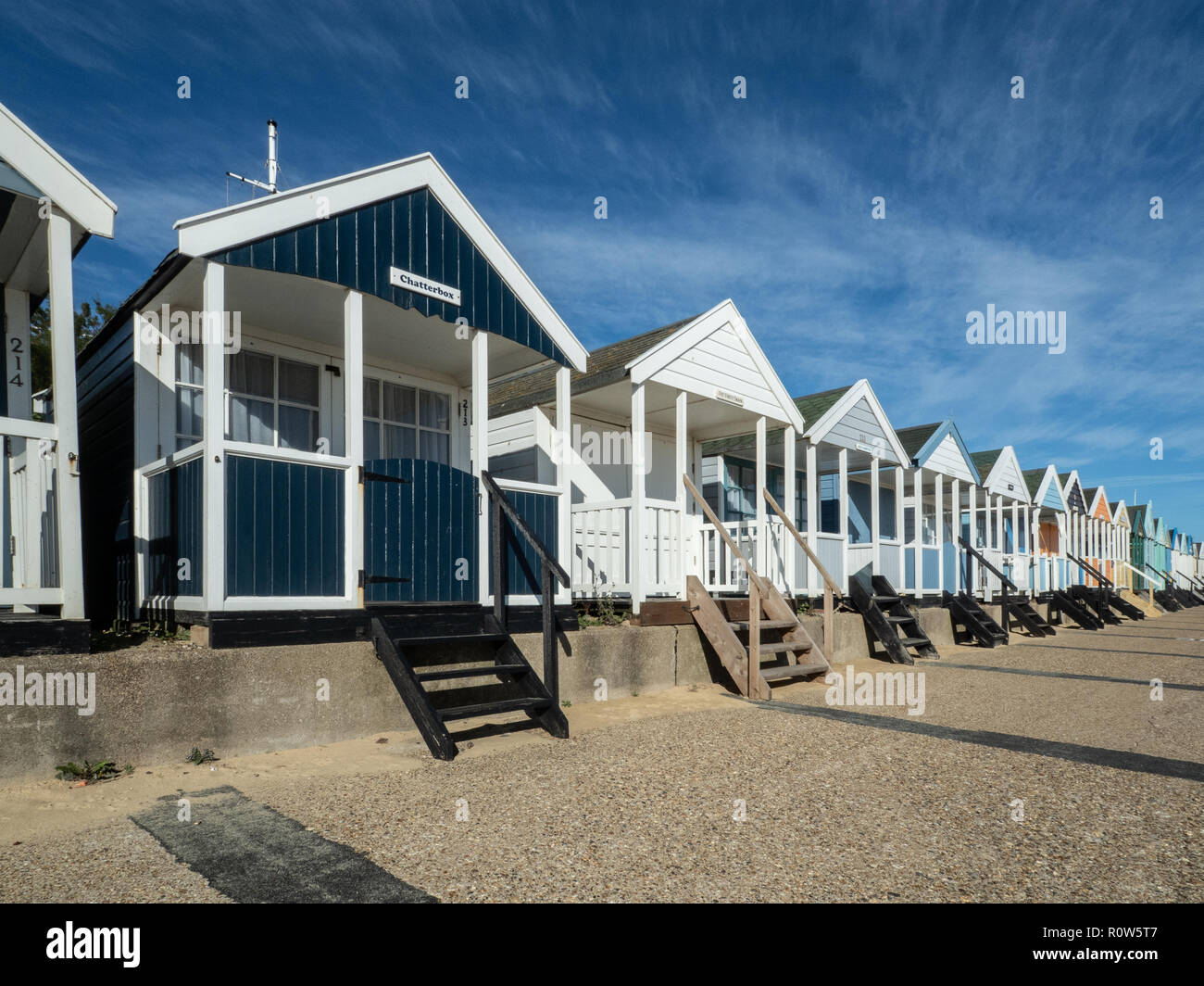 A row of brightly coloured beach huts along the seafront at Southwold against a bright blue sky Stock Photo