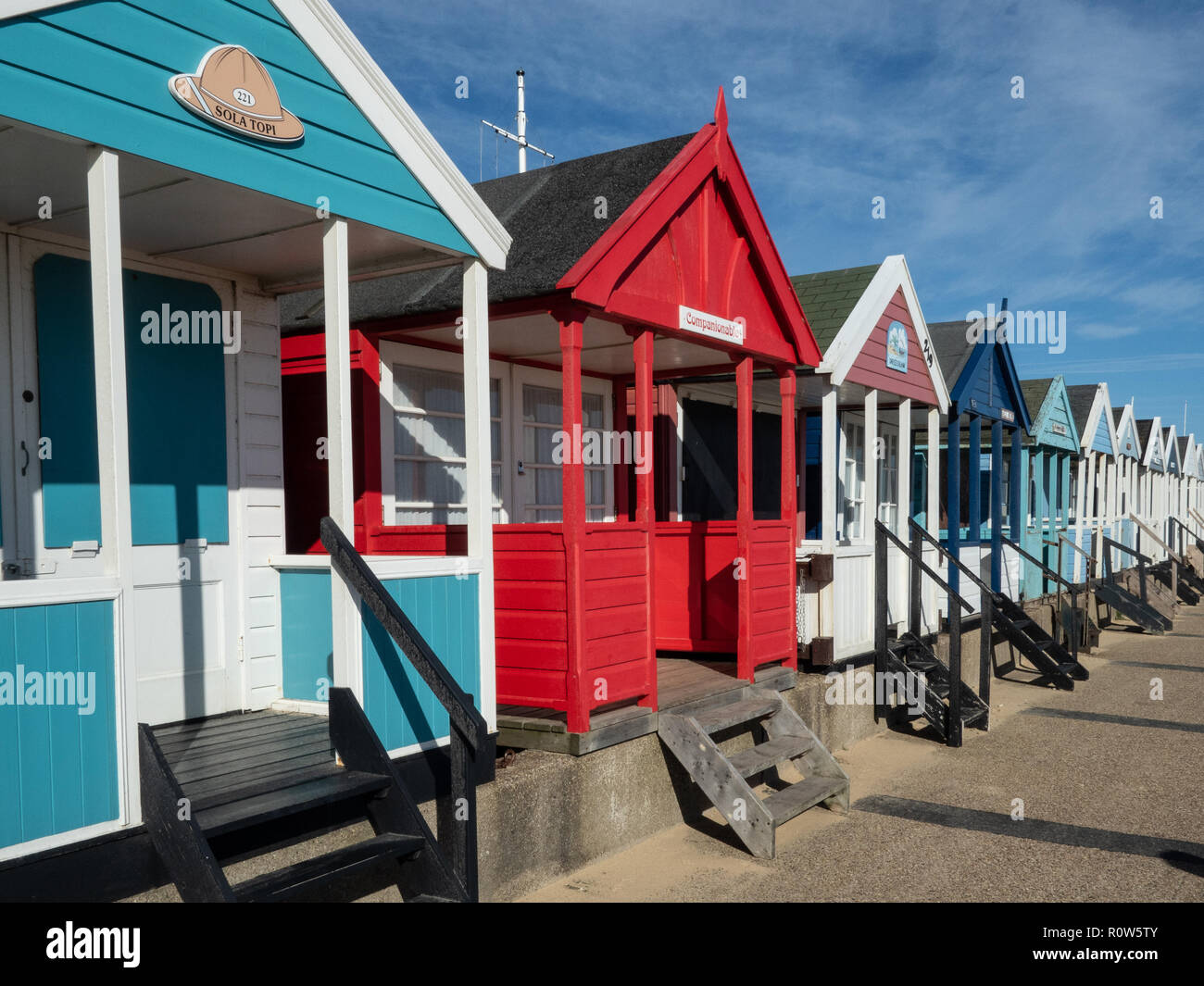 A row of brightly coloured beach huts along the seafront at Southwold against a bright blue sky Stock Photo