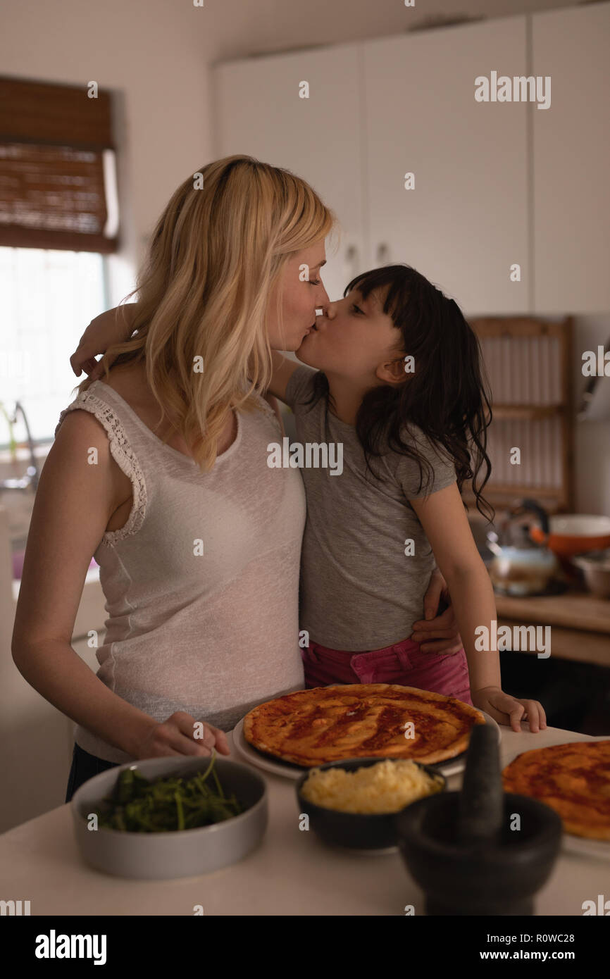 Mother kissing her daughter while preparing food in kitchen Stock Photo