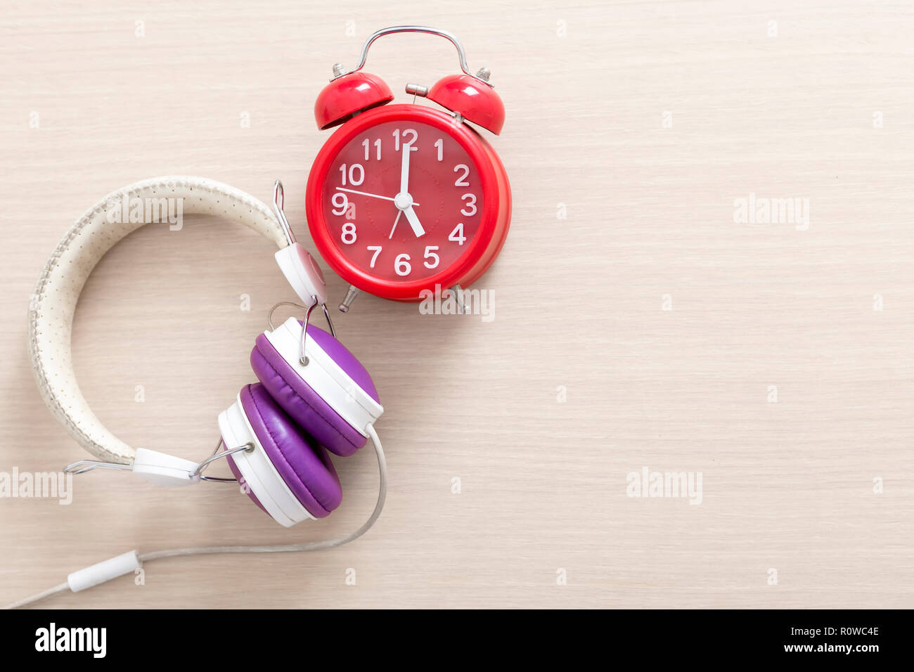Red alarm clock and headphone on wood table with free copy space for text. Education and music concept. Stock Photo