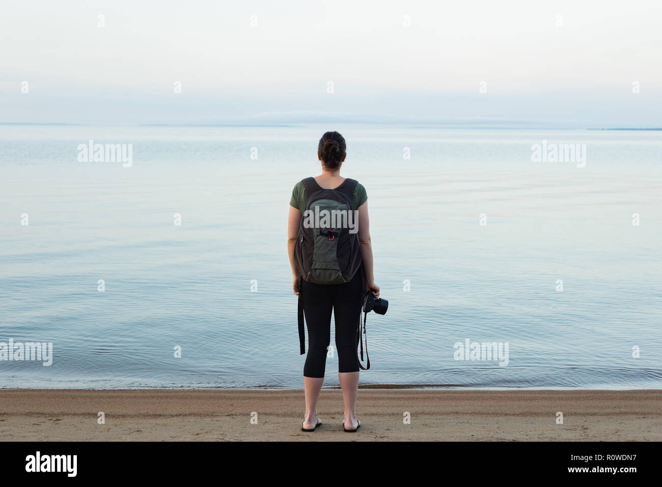 Woman standing with backpack and camera on the beach Stock Photo - Alamy