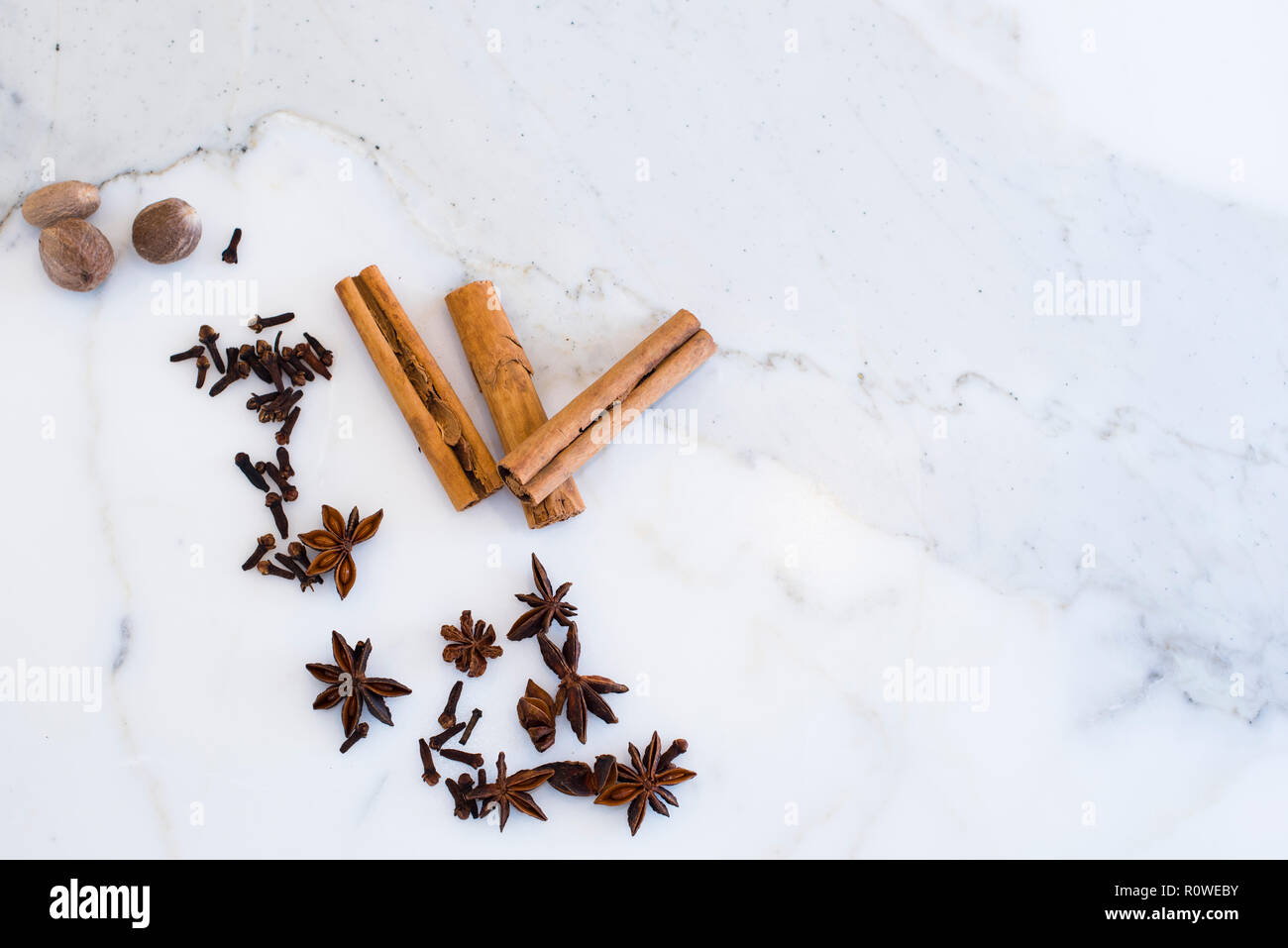 Variety of spices including cinnamon, nutmeg, cloves and star anise on calacatta marble kitchen countertop, top view Stock Photo