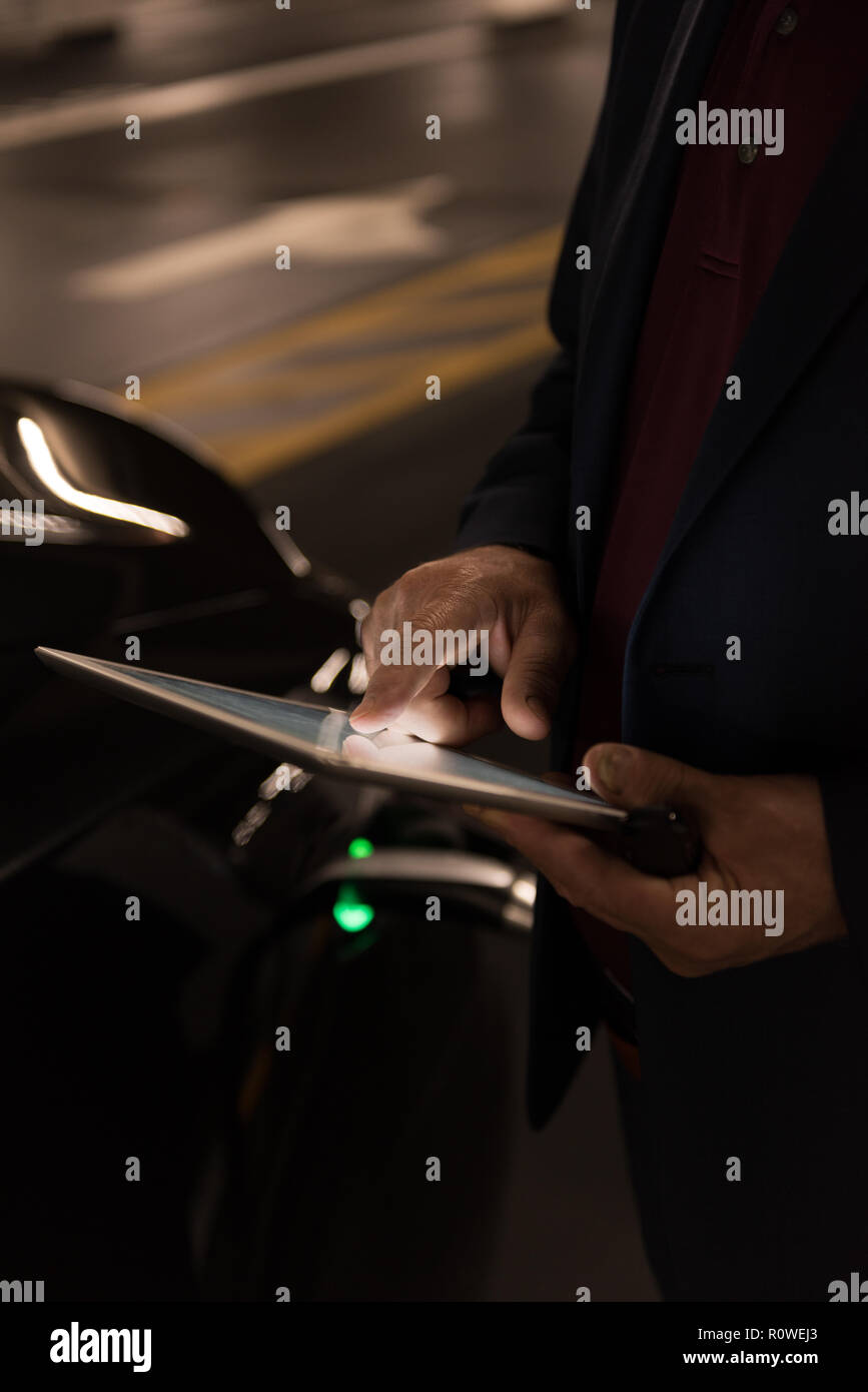 Businessman using digital tablet while charging electric car Stock Photo